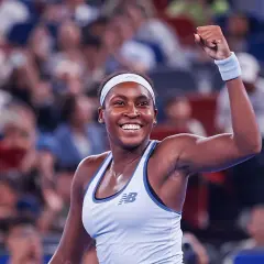 Uśmiechnięta gauff tenisistka z zaciśniętą pięścią w geście triumfu, na tle rozmazanej publiczności.