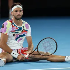 Grigor Dimitrow, tenisista, siedzi na korcie z rakietą w dłoni, zmęczony po meczu.