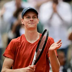 Tenisista w pomarańczowej koszulce i czapce z daszkiem, z rakietą w dłoni, dziękuje publiczności po meczu ATP 250.