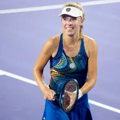 Uśmiechnięta hiszpańska tenisistka w sportowym stroju, z rakietą w dłoni, na fioletowym korcie.