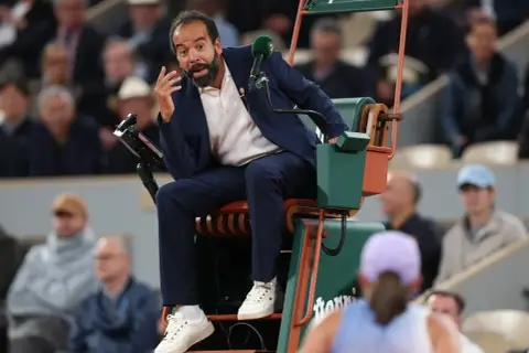 Sędziowie tenisa ziemnego WTA w akcji. Sędzia na krześle z mikrofonem, gestykuluje do gracza.