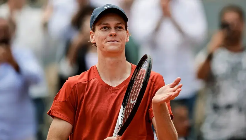Tenisista w pomarańczowej koszulce i czapce z daszkiem, z rakietą w dłoni, dziękuje publiczności po meczu ATP 250.