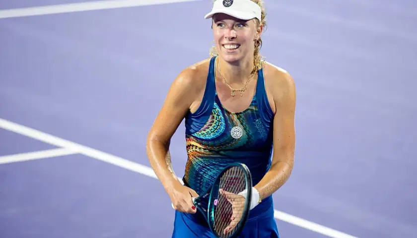 Uśmiechnięta hiszpańska tenisistka w sportowym stroju, z rakietą w dłoni, na fioletowym korcie.