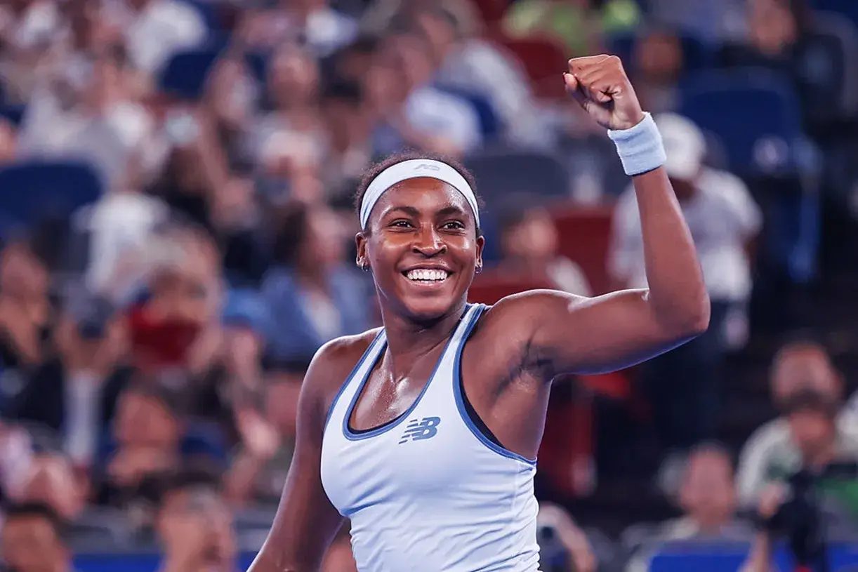 Uśmiechnięta gauff tenisistka z zaciśniętą pięścią w geście triumfu, na tle rozmazanej publiczności.