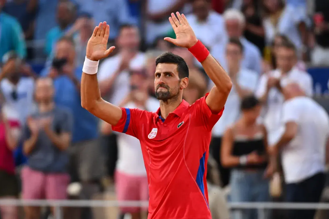 Novak Djoković w czerwonej koszulce z podniesionymi rękami, pozdrawia publiczność po zwycięstwie w turnieju WTA 500.