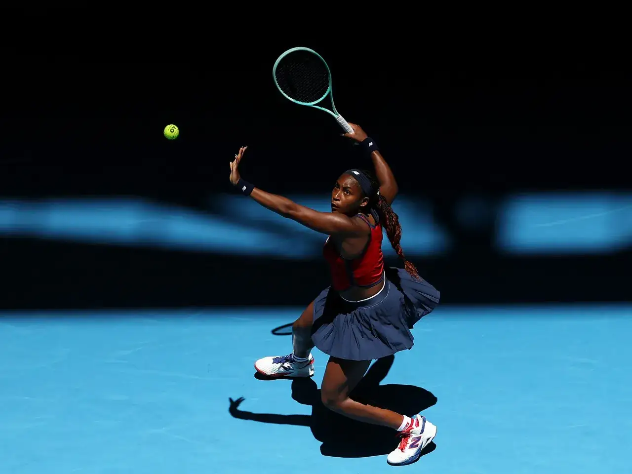 Gauff tenisistka w akcji, uderza piłkę rakietą na niebieskim korcie.