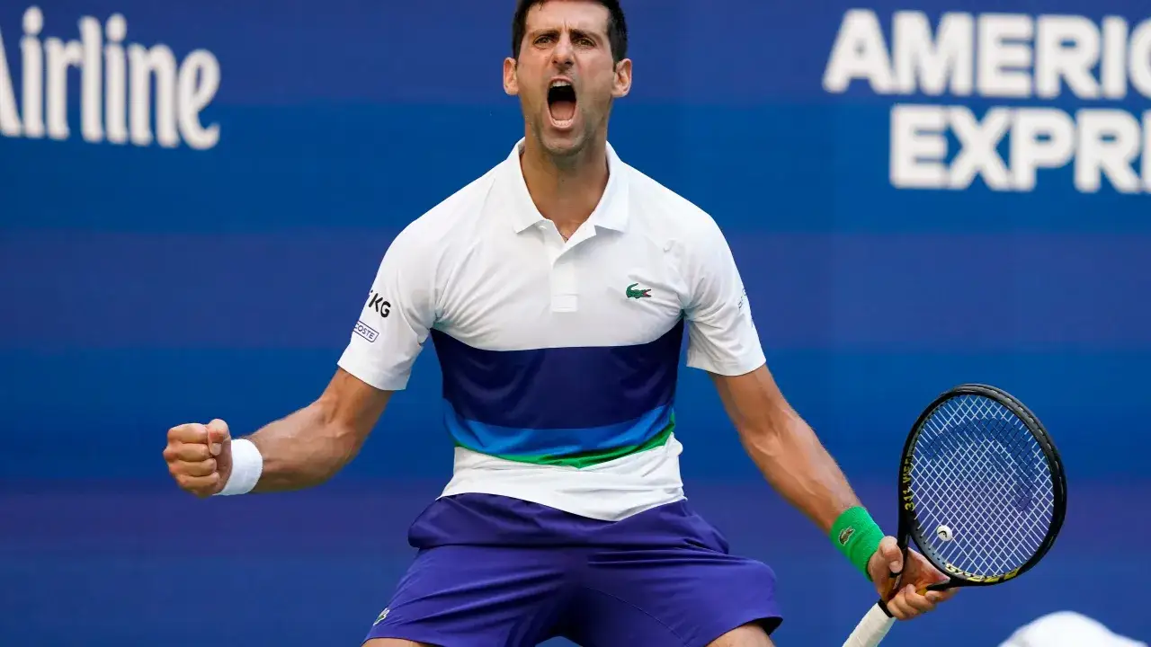 Tenisista Djokovic krzyczy z radości, zaciskając pięść. W tle widać napisy