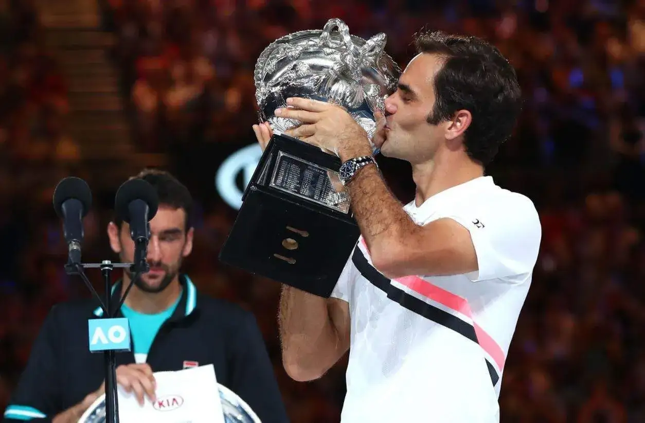 Roger Federer całuje puchar, świętując zwycięstwo jako jeden z najlepszych zwycięzców turniejów wielkoszlemowych. Marin Čilić stoi obok.